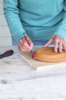 Woman marking the wooden board with a pencil and a terra cotta pot