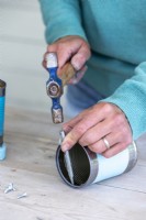 Woman using a hammer and pin punch to create a hole in the cans