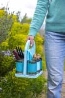 Woman carrying pastel tin can caddy containing garden tools and supplies