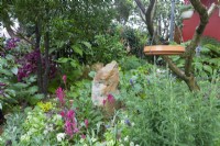 Beds of foliage and flowering plants with rock focal point and bird bath hung from tree