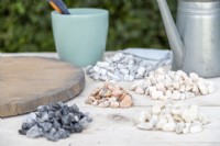 Circular stepping stone, watering can, pot of powder grout, scraper, cloth and various piles of pebbles laid out on a table