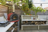 Outdoor kitchen with red pizza oven, hob and built-in wood storage