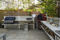 Outdoor kitchen with red pizza oven, sink hob and wood storage - Pleached trees for privacy