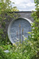 A Place to Meet Again. Hampton Court Flower Festival 2021.A circular water feature on the wall upcycles pipes and taps.