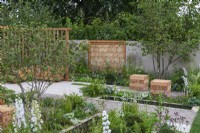 The Communication Garden. A tranquil refuge with woodland planting and native hazel trees creating a canopy. A rectangular pool and flooring laid in planking and gravel.