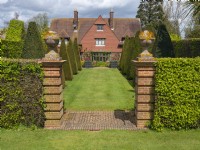 Brickwork pillars and paving marking entrance through hedge to grass path. View of Kings Walk, East Ruston Old Vicarage Gardens, Norfolk, UK.