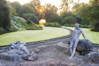 Figures of two naked males in gravel area with view to rill and lawn at sunrise. Sculptures by Jane Hazelwood. July
