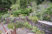 Stone retaining wall with bench, gravel with Centranthus ruber- Red Valerian - Campanula and Phormium 'Margaret Jones'