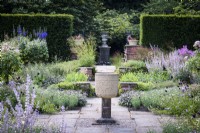 Byzantine corn grinder in the centre of Sylvia's Garden at Newby Hall, Yorkshire in July, surrounded by a formal layout including standard Rosa 'Ballerina' and purple sage.