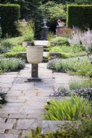 Byzantine corn grinder in the centre of Sylvia's Garden at Newby Hall, Yorkshire in July, surrounded by a formal layout including herbaceous perennials and purple sage.