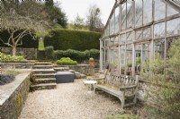 Seat against the conservatory at Lower House, Powys in March with steps leading up to terracing with clipped box and a mulberry tree.