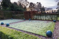 Diagonal view across the frosty lawns as the sun rises. Painted balls form man-made structure alongside the clipped hornbeam and box hedges.