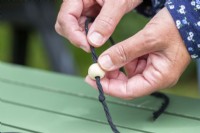 Placing a bead on the string to sit on top of the knot