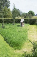 Bee hotel at orchard with young apple trees and mowed paths in the grass.