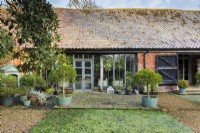 View of part of the frosty-roofed barn and the barn garden with its grass parterre and containers of clipped Phillyrea latifolia. Featuring the orangery.