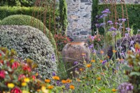 View through flowers to an empty urn amongst Buxus, Hebe and Pittosporum topiary. 