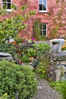 Low stone wall with wooden sculpture in a cottage front garden full of plants. 