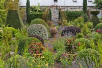 View over topiary to arch, Fuchsia triphylla 'Thalia' in pots, gravel path with Calendula officinalis and Lavandula angustifolia. Mixed topiary: Pittosporum, Hebe and Buxus.