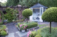 Secluded parterre garden with summerhouse. Paths and walls made of reclaimed cobbles and station platform tiles. Planted with Buxus sempervirens hedges infilled with Lavandula angustifolia, and Thuja standards