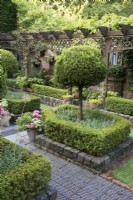 Secluded parterre garden with paths and walls made of reclaimed cobbles and station platform tiles. Planted with Buxus sempervirens hedges infilled with Lavandula angustifolia, and Thuja standards