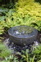 Layered slate water feature surrounded by lush planting including hostas, ferns and grasses in July