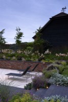 Contemporary garden in dusk with lights inset into steps of Lucca brick pavers, and brick retaining wall in July. 