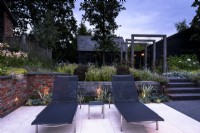 Contemporary garden in dusk with lights inset into steps and brick retaining wall in July. 