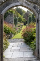 Looking through arched doorway down long borders in late summer garden