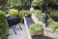 Corner of patio with bench made of reclaimed floor heating church grill and wall planted with alpines 