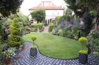 View of garden with curving lawn, paths made from reclaimed cobbles and summer flowerbeds