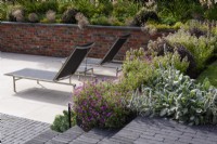Steps of Lucca brick pavers made by Chelmer Valley lead up from a terrace of Duomo Sabbia porcelain tiles softened by Stachys byzantina 'Silver Carpet' and Geranium Ã— riversleaianum 'Russell Prichard' in July.