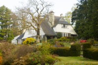 The Arts and Crafts style house on a hill at High Moss surrounded by mixed borders and a topiary hedge - Taxus baccata and a large oak tree - Quercus