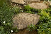 A stepping stone with a wave pattern surrouned by grasses and ferns in the Guangzhou China: Guangzhou Garden,  winner of the best show garden award.
