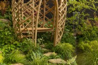 A laminated bamboo grid structure  with a seat beside a fountain surrounded by a pool in a woodland dell in the Guangzhou China: Guangzhou Garden winner of the best show garden award.