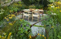 A dining area on a paved terrace surrounded by autumn planting set in wooden containers in the Parsley Box Garden, an edible sanctuary garden.