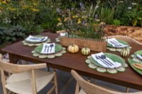 The garden table is laid for lunch and has a flower arrangement  as a centre piece. 
