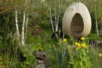 An egg shaped hide made from bent oak beside a stream and surrounded by Betula pendula and perennials including: Rudbeckia laciniata 'Herbstonne' and Calamagrostis brachytrica - Korean feather reed grass in the Yeo Valley Oganic Garden.