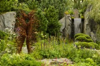60 Degrees East, a garden between continents, a figurative metal sculpture beside a waterfall on a hillside surrounded by European and Asian planting.  Sculptures by Penny Hardy