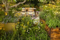 A dining area surrounded by perennials in wood and metal containers.  