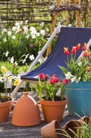 Containers with spring flowers and a deck chair on a patio.