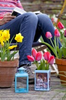 Woman relaxing on chair surrounded by tin box with red tulips and containers of tulips and daffodils.