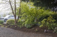 Layers of deciduous and evergreen trees, shrubs and perennials filter view of home and private sitting area from street