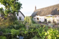 View of the garden with pond in foreground backed by thatched houses 