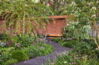 Pathway through mixed borders to the bench and wall panel. The Florence Nightingale Garden, RHS Chelsea Flower Show 2021