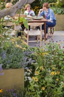bed with sanguisorbas, rudbeckias, achilleas, catmint and salvias. People relaxing in the garden in the background. The Parsley Box Garden at Chelsea Flower Show 2021