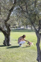Young woman with her dog in the park amongst Olive trees. Lisbon, Portugal, September.