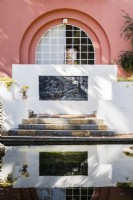 The serpent lake with view to the house and decorative panel of painted cement in wall above steps, reflected in the pool.