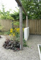 Wooden fence. Dividing garden with small, low, white wall and wooden pergola. Gravel surface. Rudbeckia and Heuchera in the border.