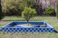 The citrus orchard in the lower garden with fruit tree in square raised beds surrounded by geometric shaped pool. Walls and pool faced with brightly coloured glazed tiles. Lisbon, Portugal, September.