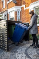 Garden owner, woman in her front garden placing wheely bin into garden store